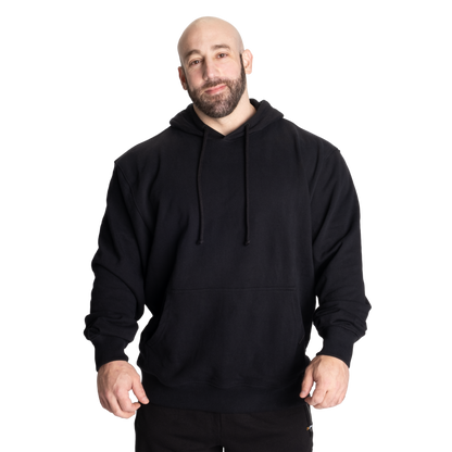 A man wearing a plain black pullover hoodie with drawstrings and a front kangaroo pocket, standing against a solid white background.