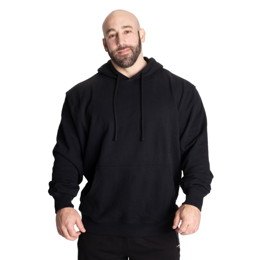 A man wearing a plain black pullover hoodie with drawstrings and a front kangaroo pocket, standing against a solid white background.