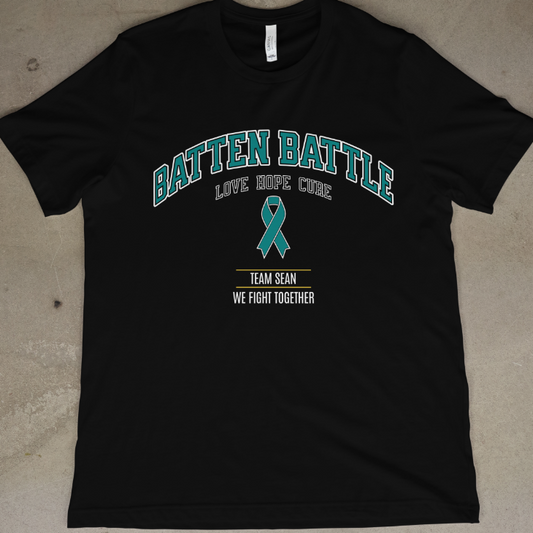Black t-shirt with 'Batten Battle' text and teal ribbon on a concrete floor.