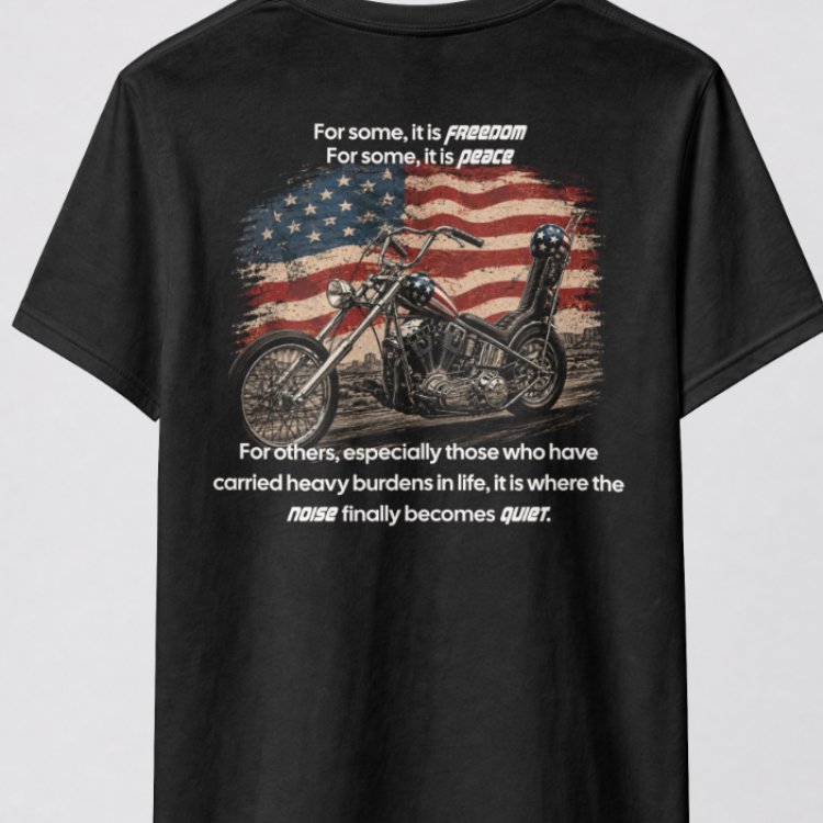 A black short-sleeve t-shirt hanging on a black hanger from a metal rack, showing the back of the shirt with a graphic of a chopper motorcycle over an American flag and a quote printed in white.