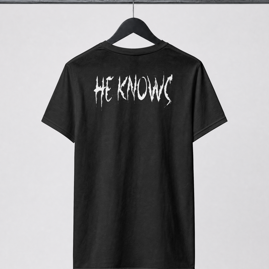 Black t-shirt with 'HE KNOWS' text on a hanger against a white background